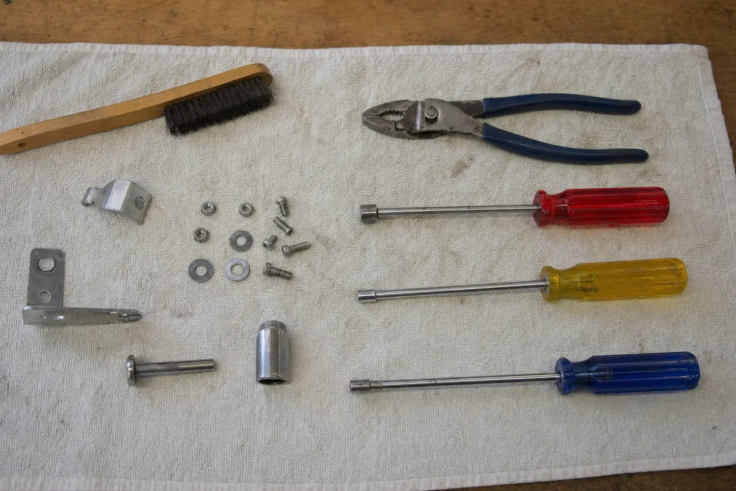 Brush, pliers and three nut drivers on a white cloth with two brackets, a sleeve and loose screws, nuts and washers
