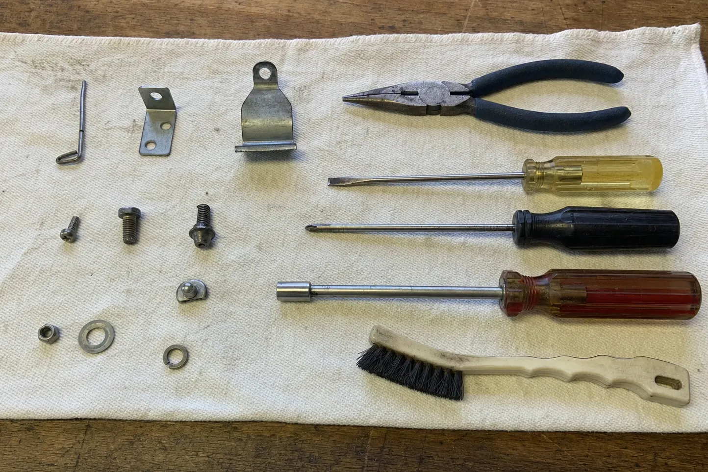 Retaining clip, two brackets and their fixings laid out on canvas with needle-nose pliers, drivers and a nylon brush