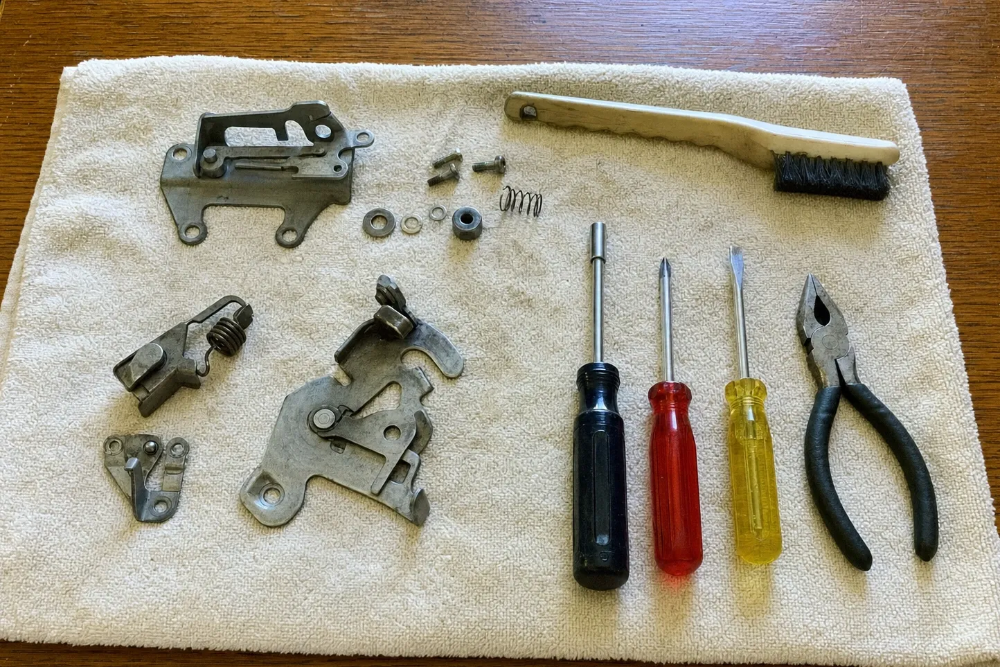 Oven door latch mechanism stripped into four pieces with its springs and cams, drivers and pliers alongside
